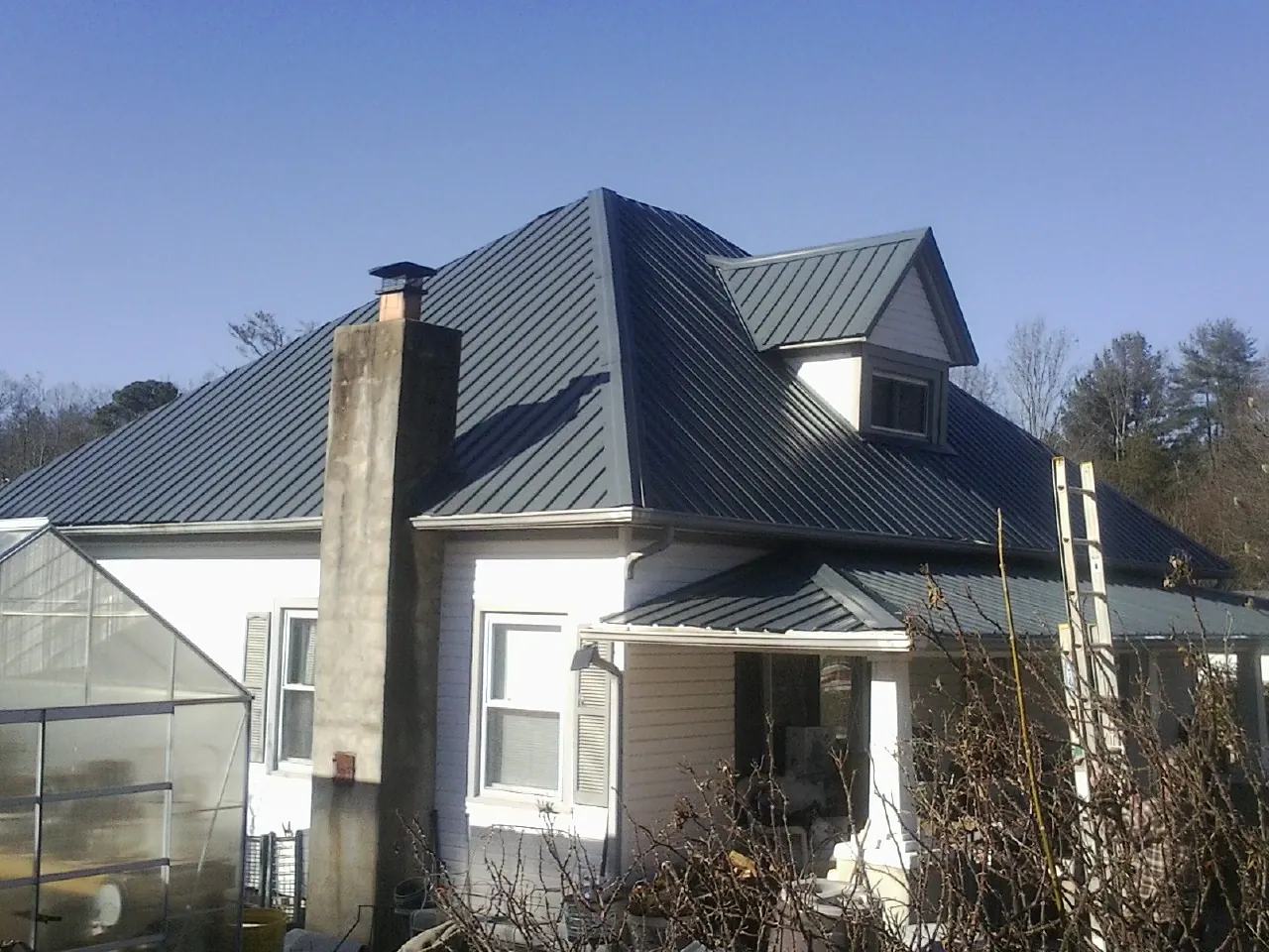 Dark blue standing seam metal roof on a white farmhouse with dormer — Slate & Tile Roof Repair by Roofing Brothers in Crete