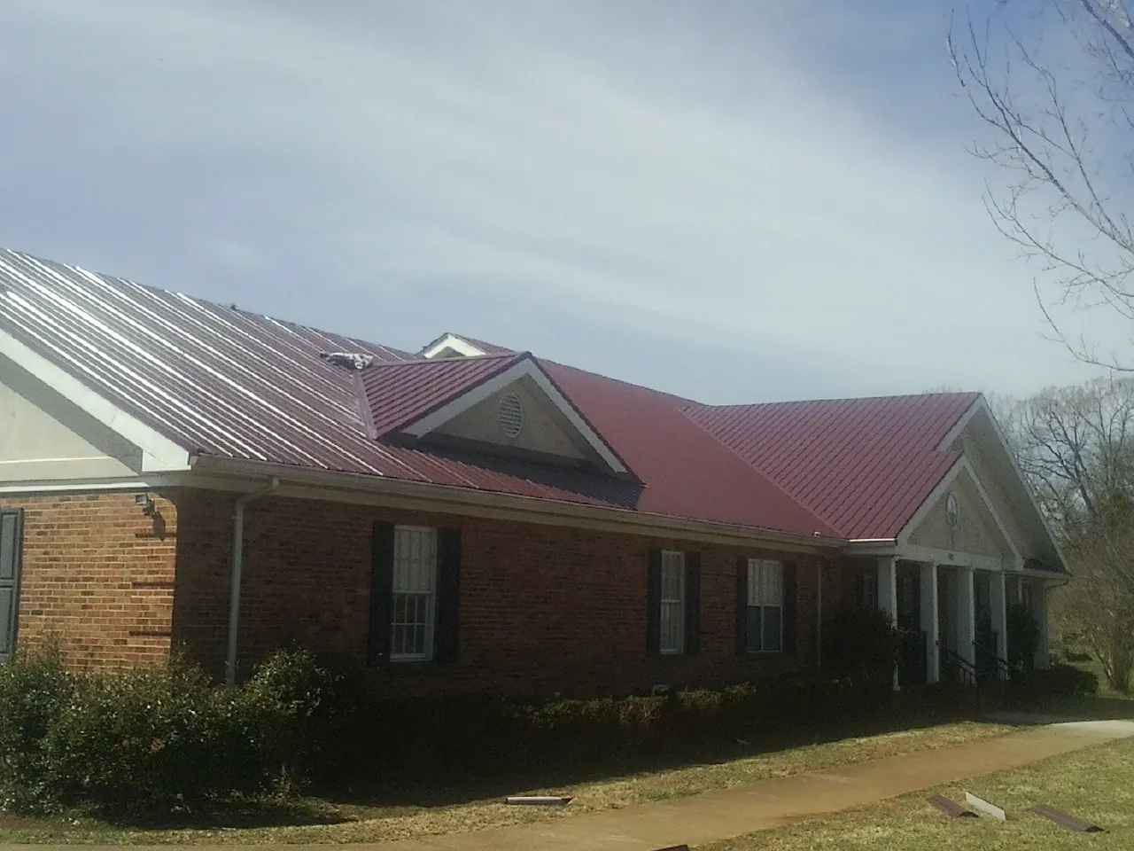 Red metal roof with gabled entries on a long brick building, from a Hail Damage Roof Repair job in Crete